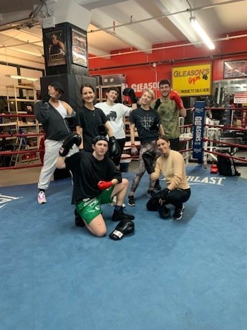 Group of women in boxing gloves and workout attire inside a boxing gym, posing for a photo.