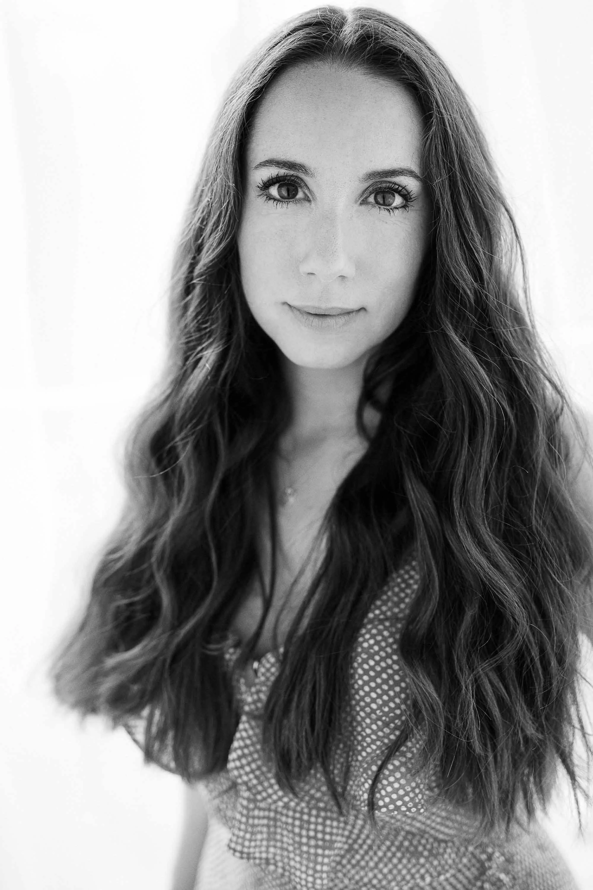 Woman with long wavy hair in patterned top, smiling gently at camera. Relaxed and professional branding portrait.