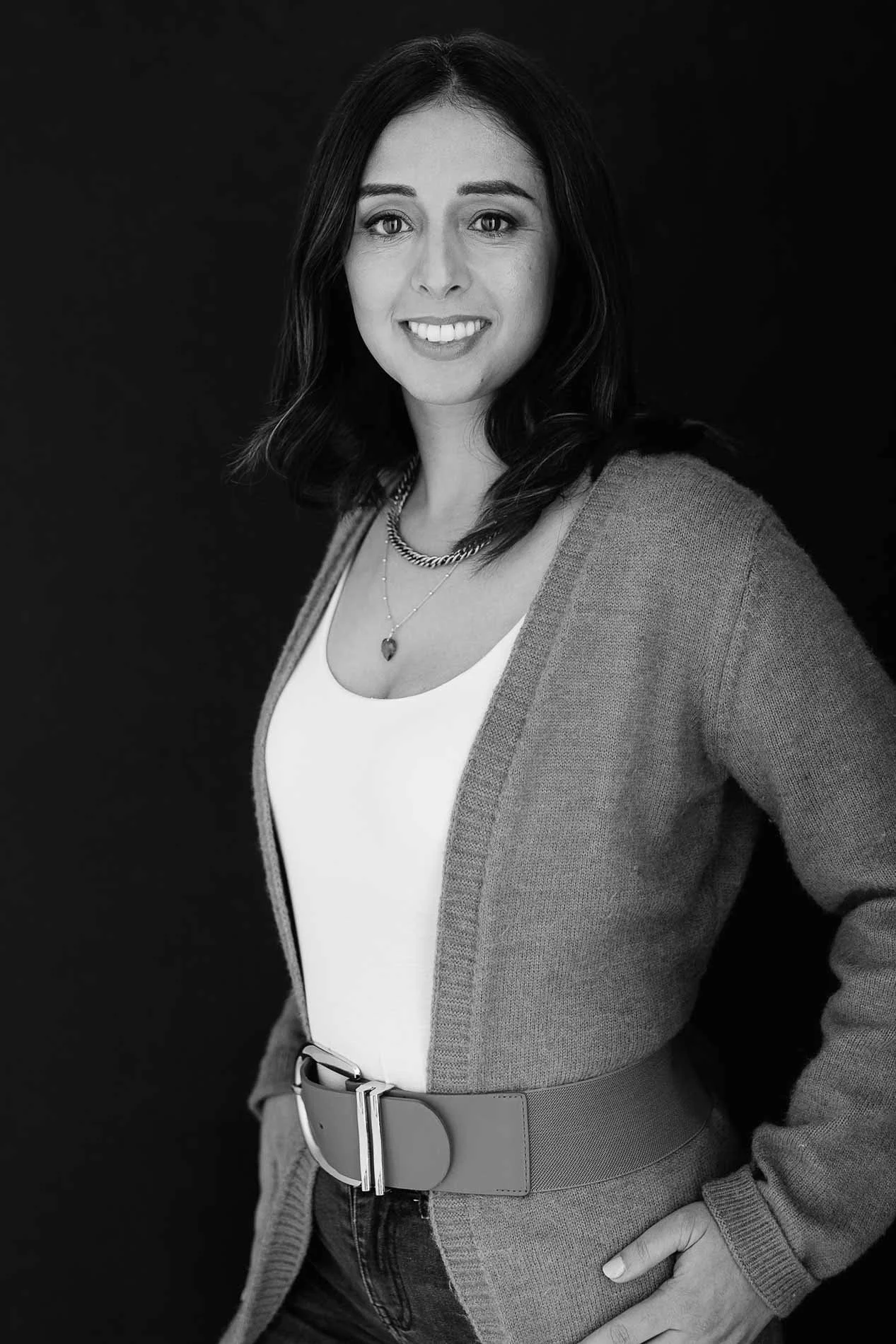 Smiling woman in cardigan and layered necklaces, standing confidently. Friendly and warm personal branding image.