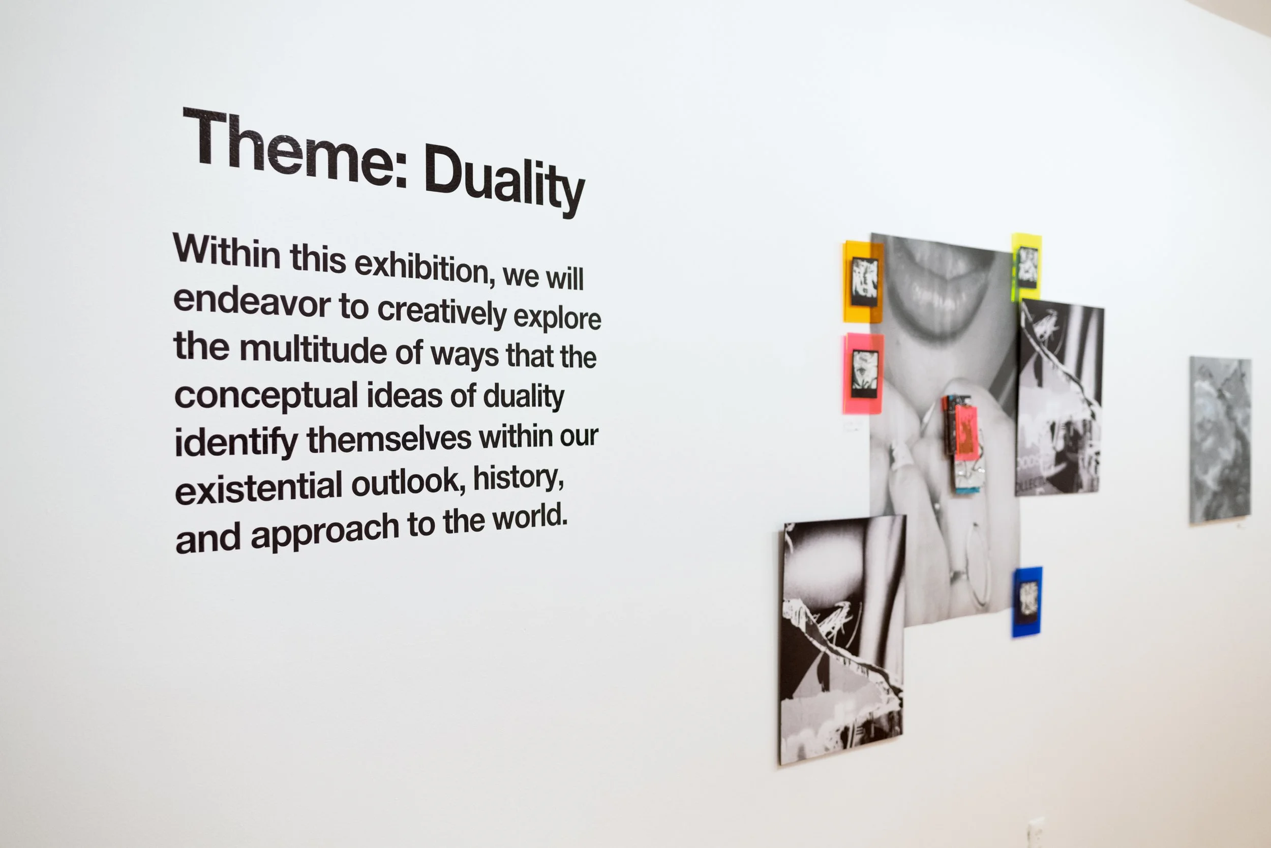 Exhibition wall with text titled 'Theme: Duality'; explanatory paragraph about exploring duality in worldview, history, and approach; black and white photographs, some with colorful borders, arranged on the wall.
