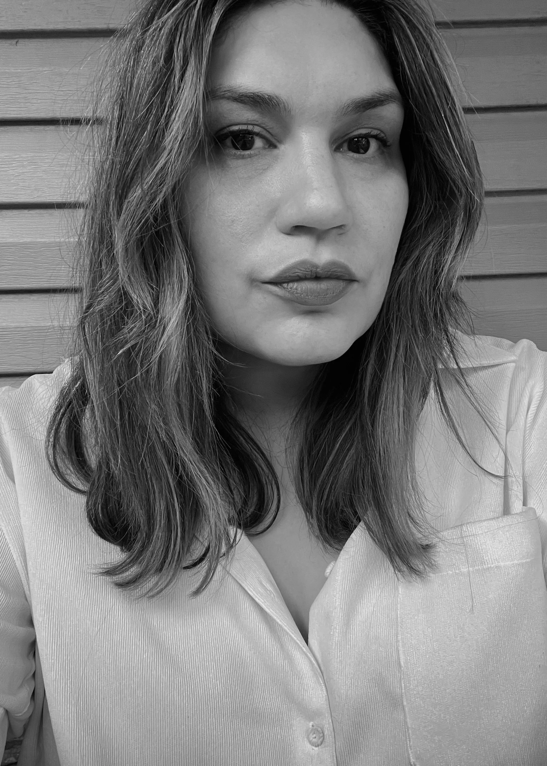 Black and white portrait of a woman with wavy hair, looking directly at the camera, with a wooden background.