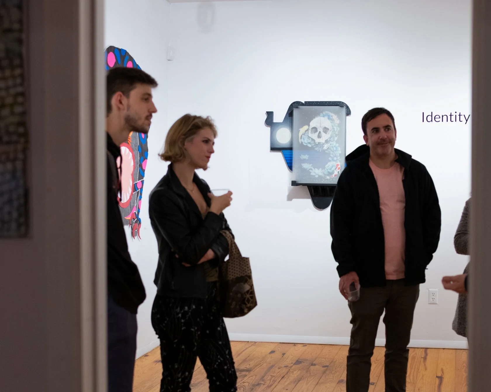 People viewing artwork in a gallery. The wall has a digital art piece with a skull and the word 'Identity' written beside it.