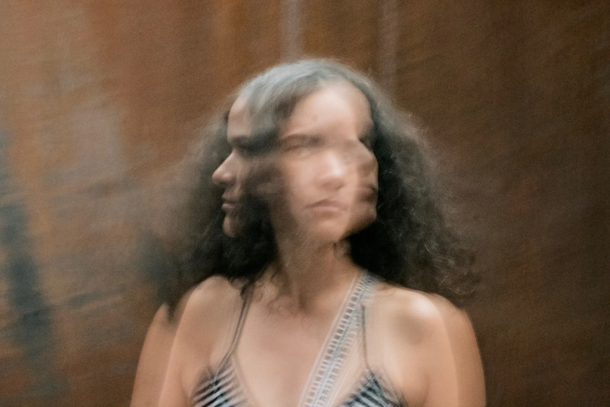 A woman with dark, curly hair wearing a striped tank top, with her face appearing blurred and distorted.