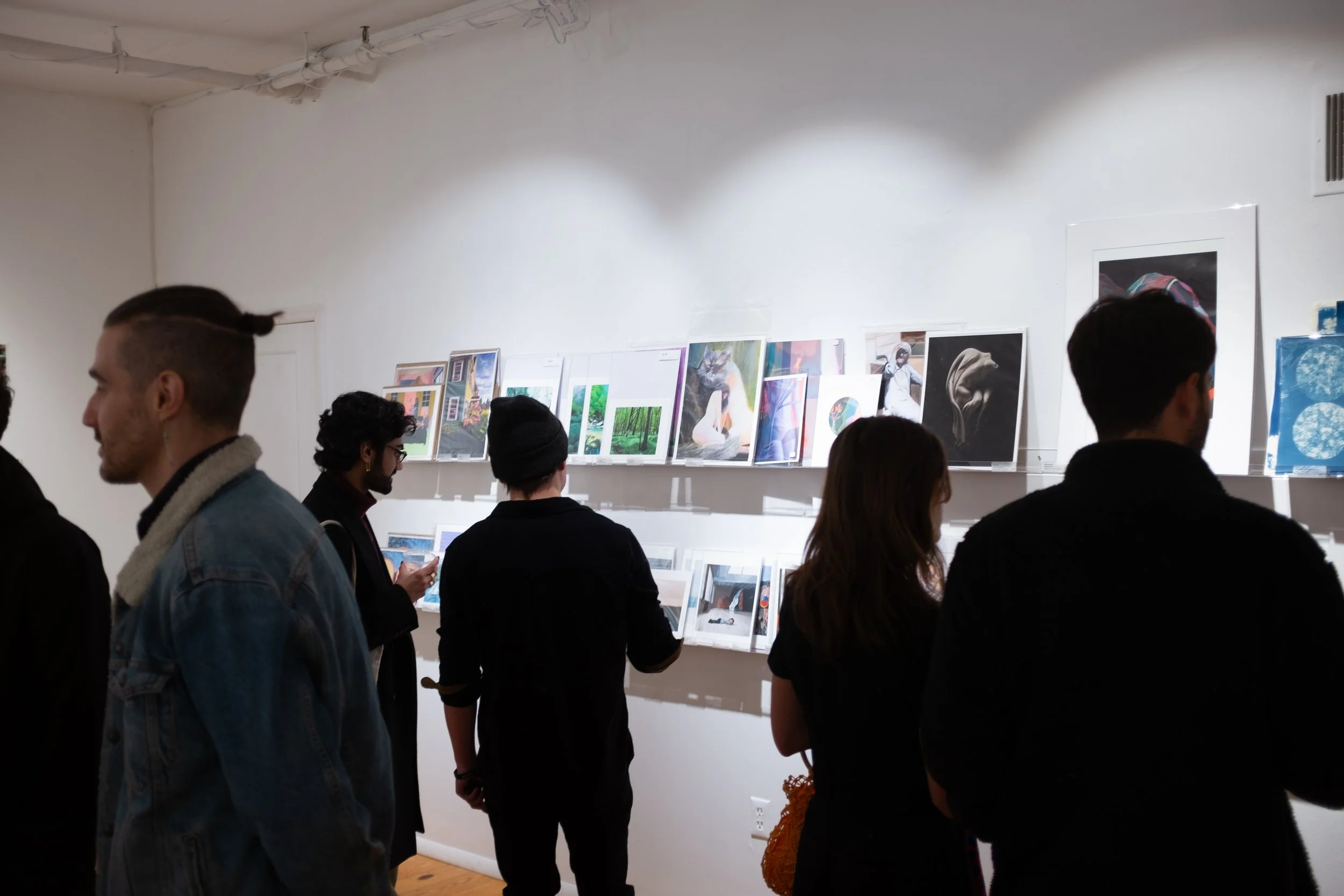 People viewing artwork in an art gallery, with artworks displayed on a white wall.