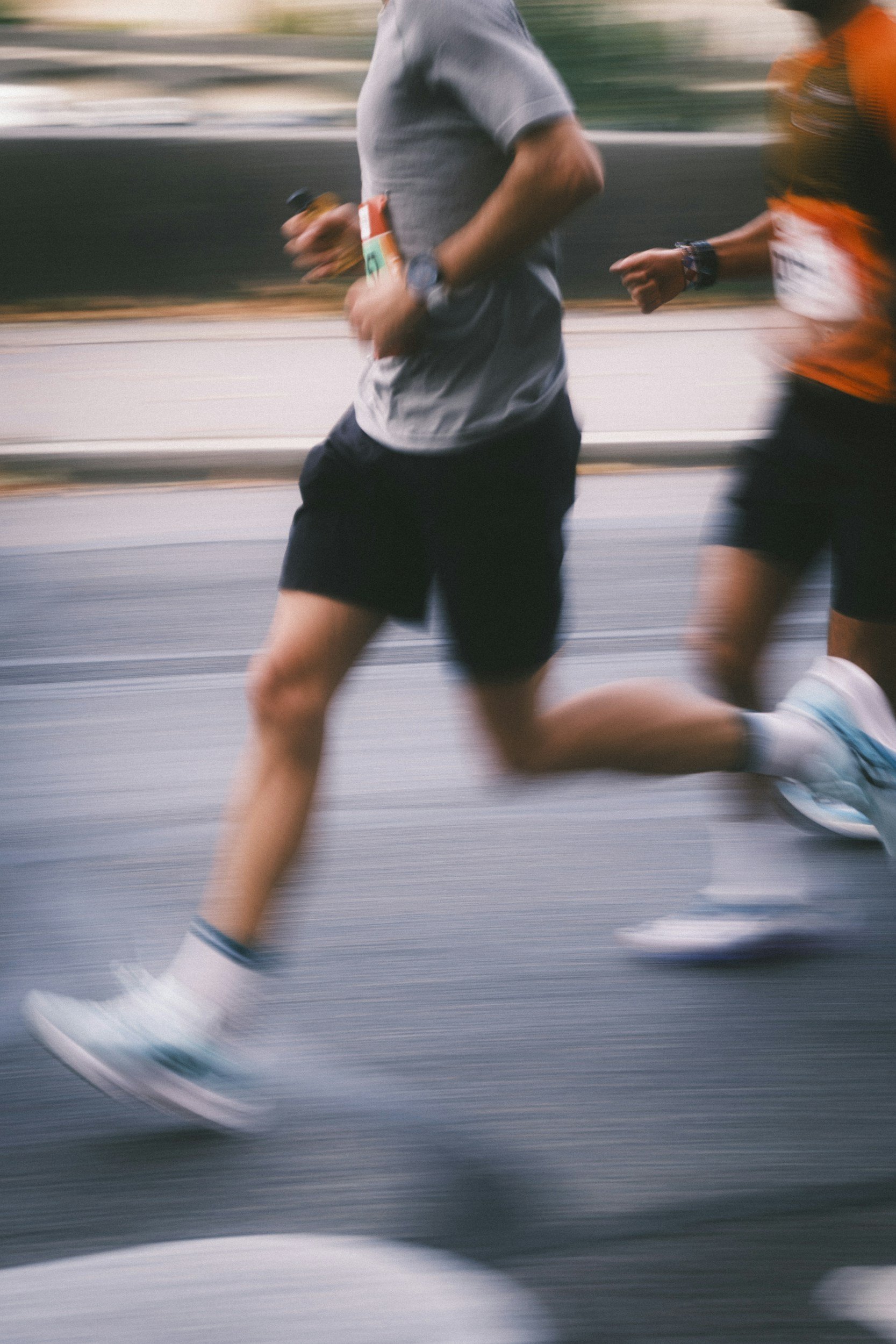 Blurry image of a male runner wearing a gray shirt, black shorts, and race bib running in a race