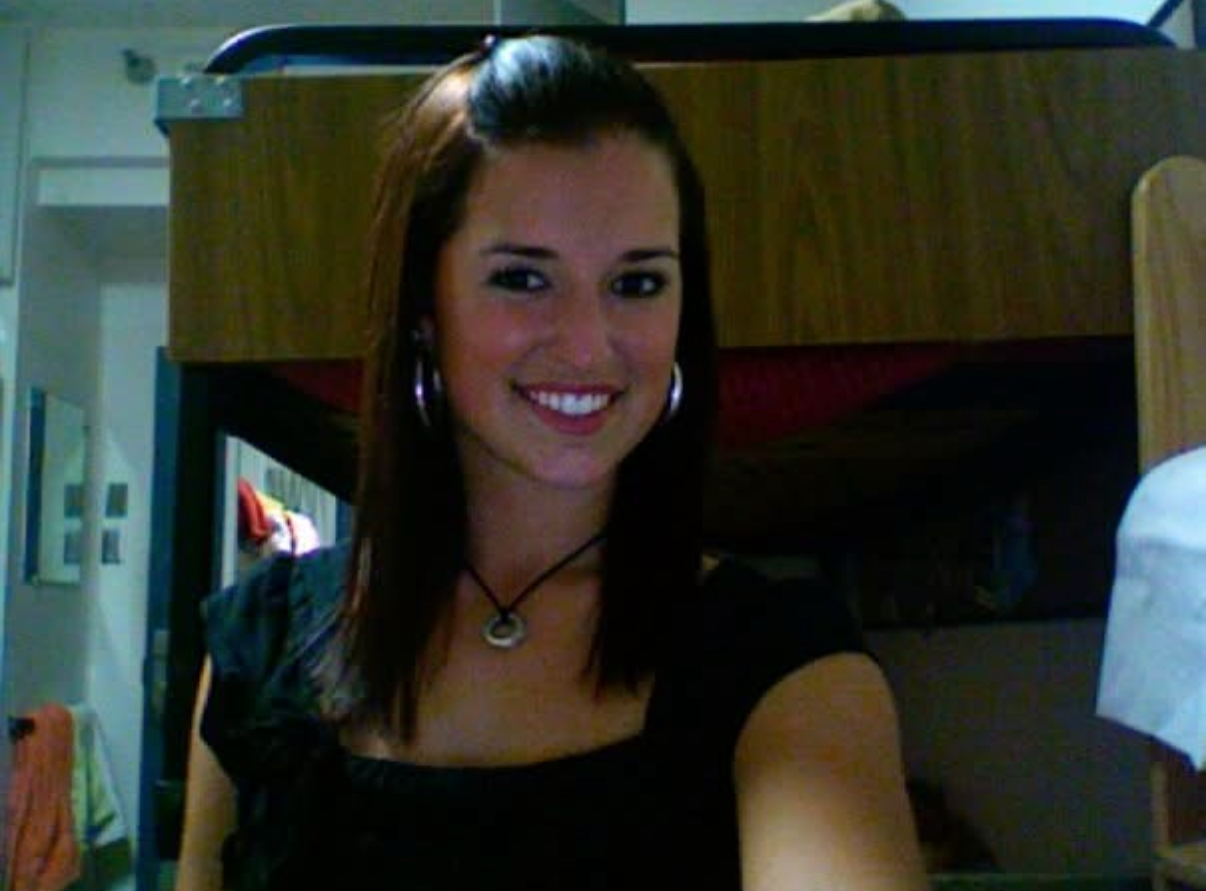 Kait with straight brownish reddish hair sitting in her college dorm room