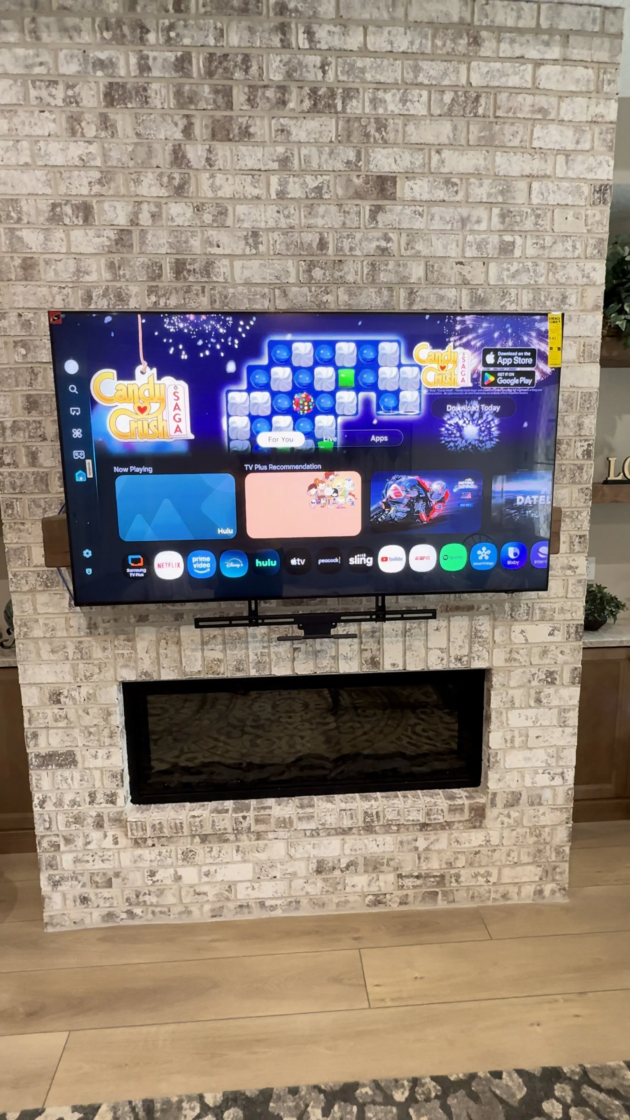 A flat-screen TV mounted above a fireplace with a brick surround, displaying a streaming service interface.