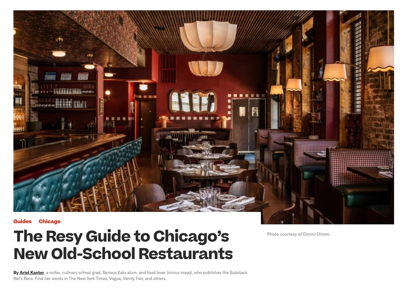 Interior of a cozy restaurant with a bar counter on the left, tables set with plates and glasses, booth seating along the right side, warm lighting, exposed brick walls, and wooden accents.