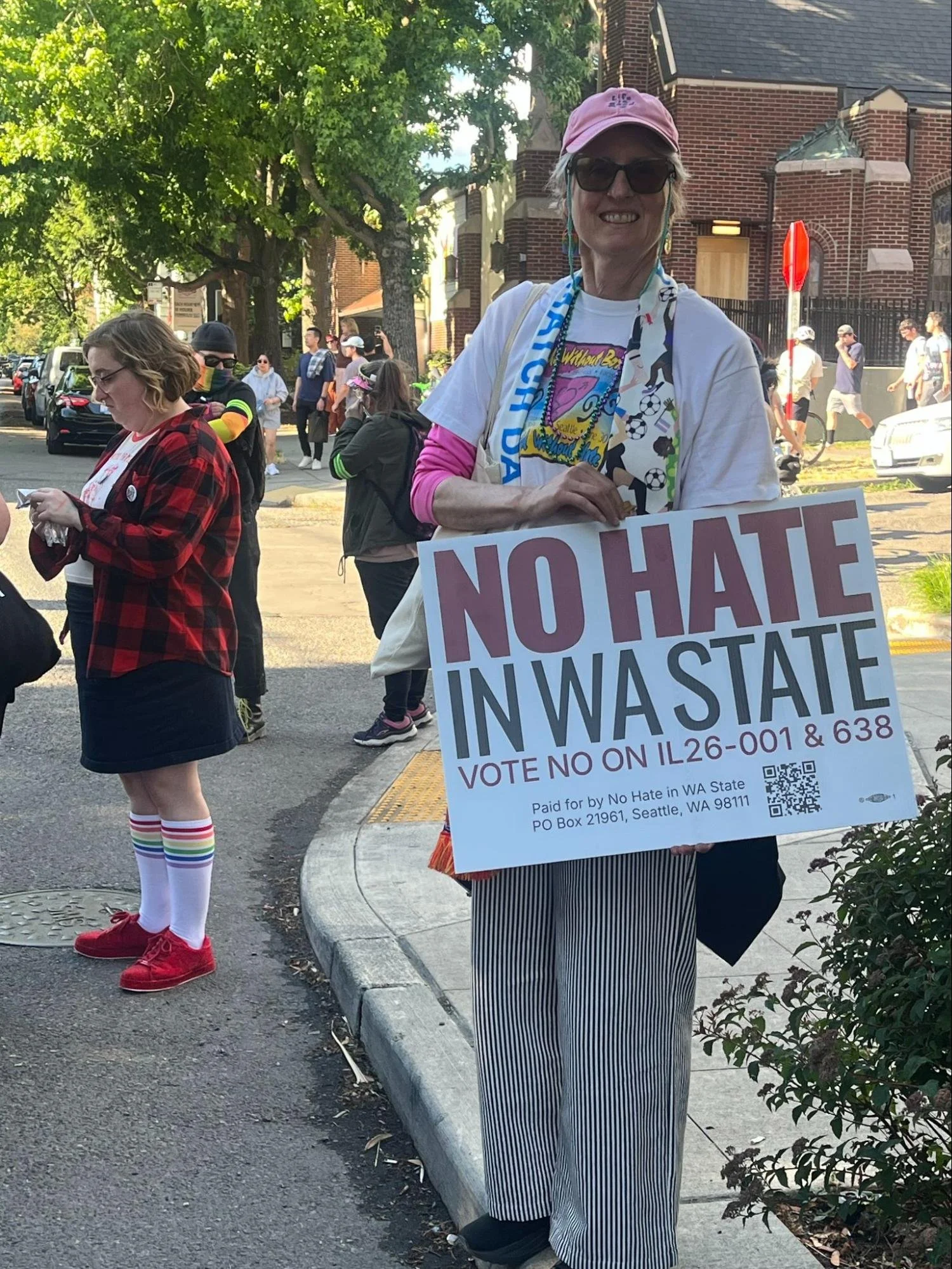 A person in a pink hat holding a sign that reads 'NO HATE IN WA STATE, vote no on I-26...'