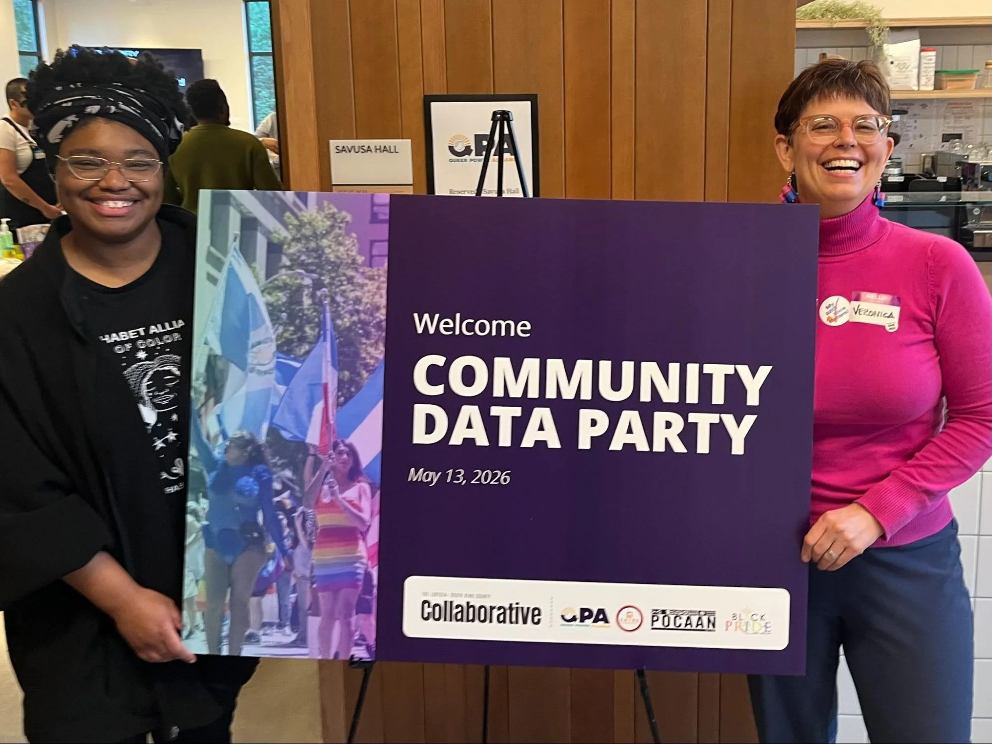 Veronica Smith and Kory Higgs pose together holding a sign reading “Welcome: Community Data Party,” dated May 12, 2026.