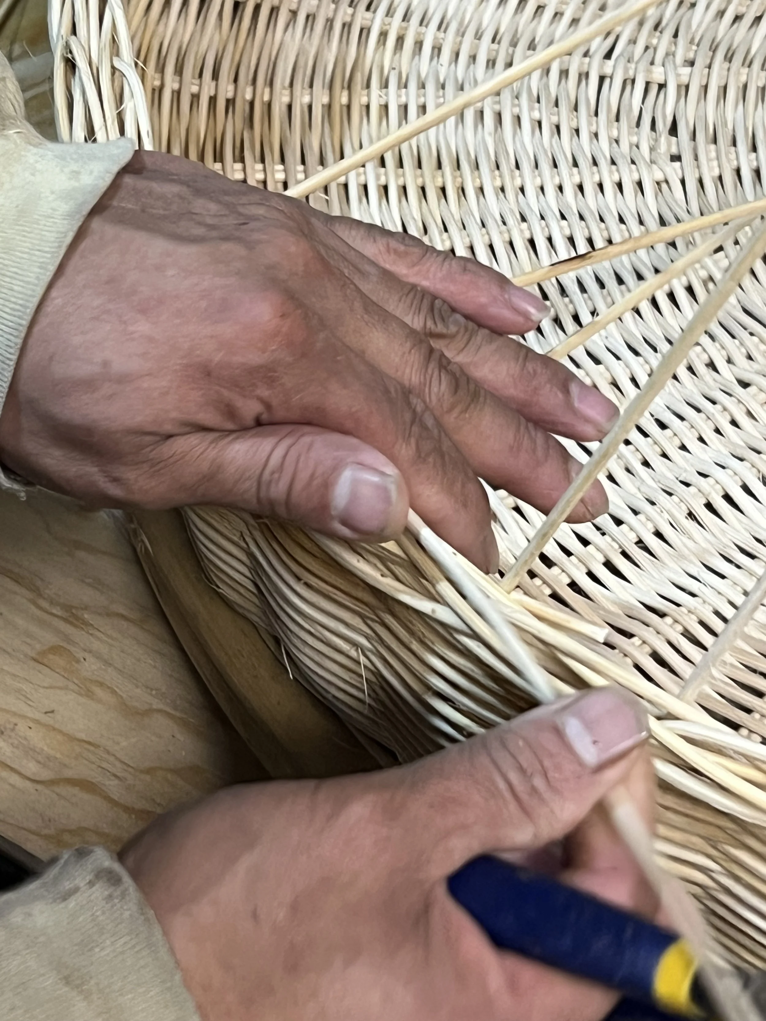 Una mano humana sostiene un trozo de madera en una canasta de mimbre, con herramientas de carpintería y una superficie de trabajo de madera en el fondo.