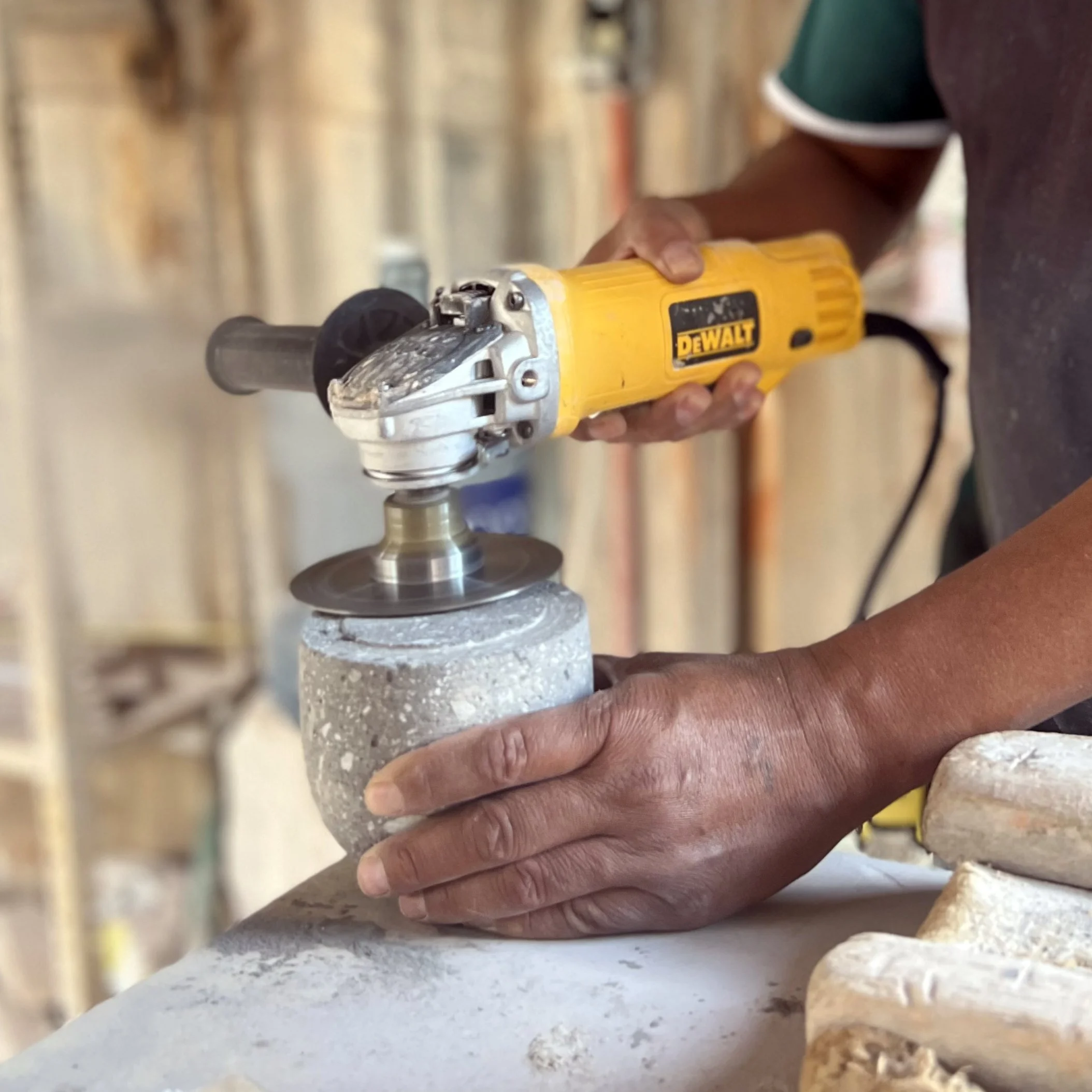 Manos de un artesano trabajando con una herramienta eléctrica en una pieza de piedra en un taller.