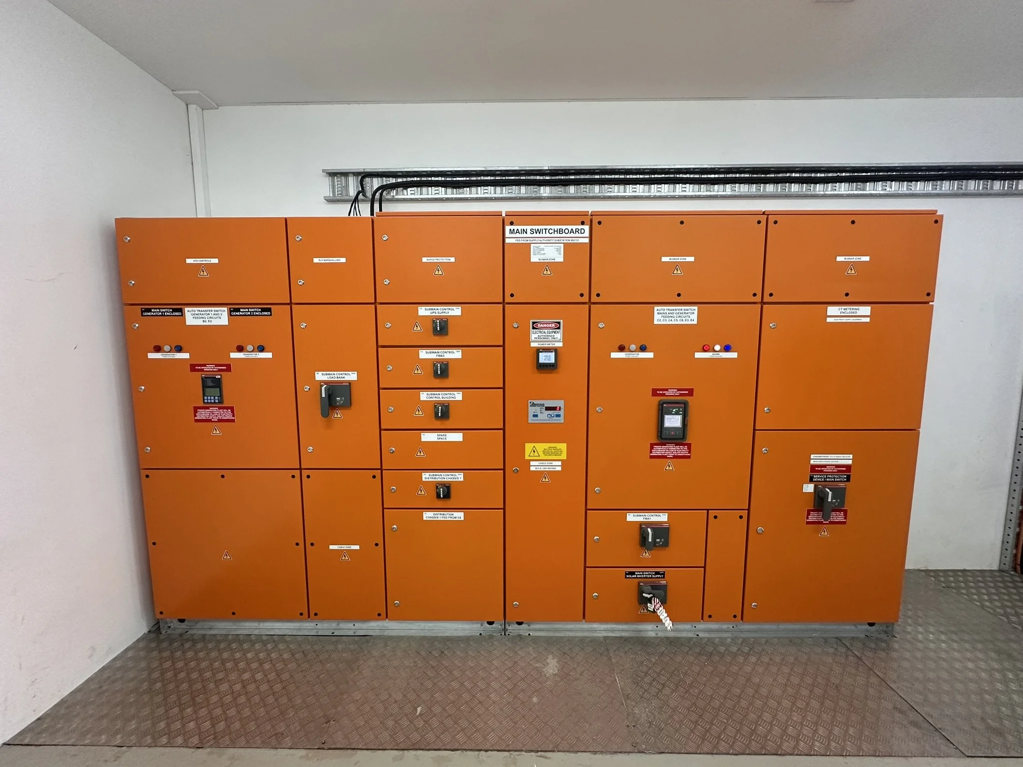 Orange electrical control panels mounted on a wall in an industrial or utility setting, with various switches, buttons, and warning labels.