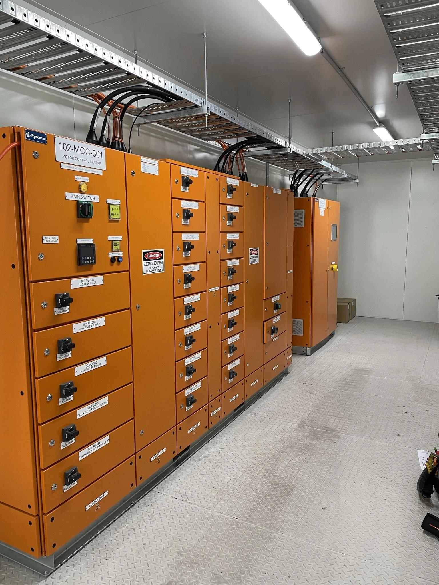An electrical control room with orange control cabinets and labeled switches, enclosed in a clean, well-lit space with a tiled floor.