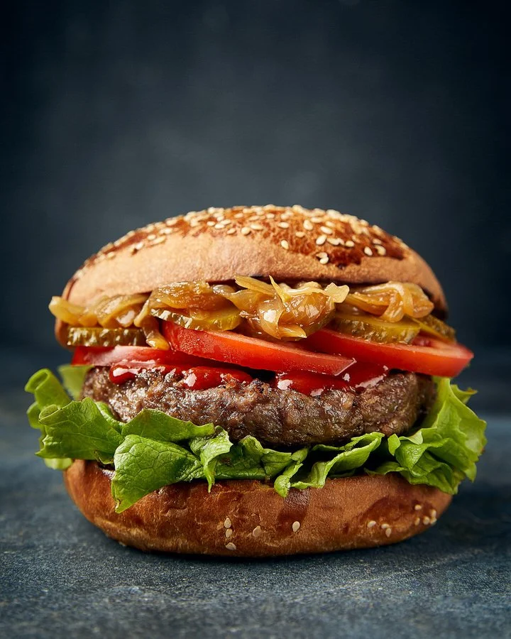 Gourmet hamburger with lettuce, tomato, pickles, caramelized onions on a sesame seed bun