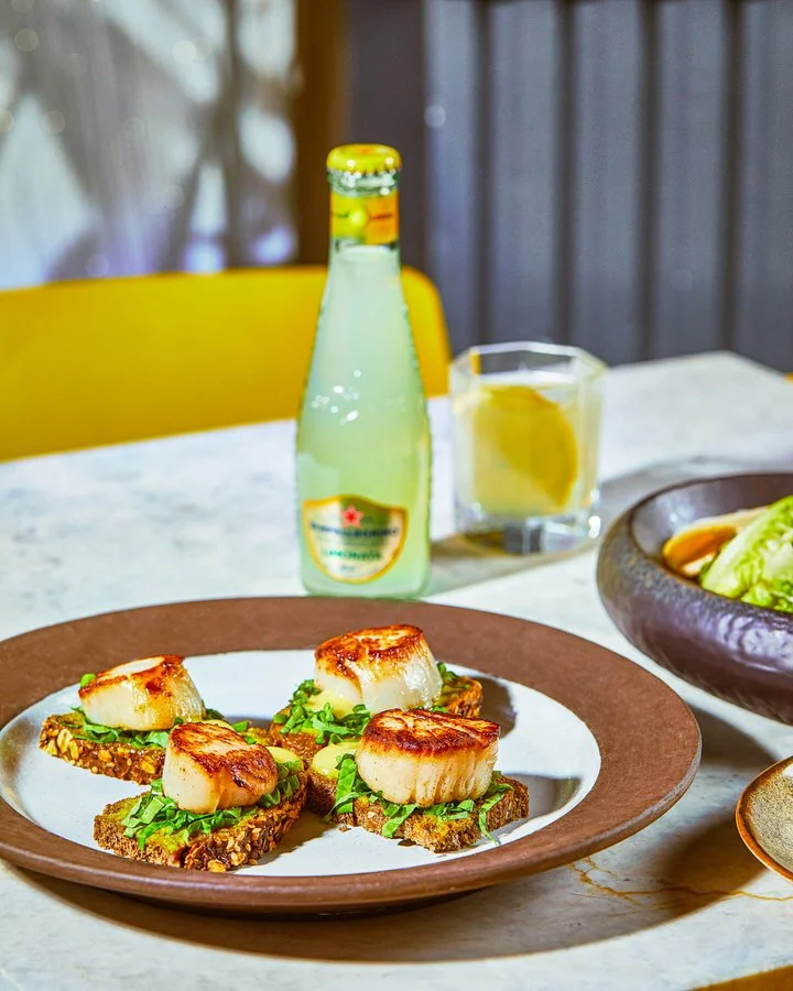 Bir şişe soda, kristal bardaklar ve beyaz seramik kaselerle süslenmiş masa düzeni.

