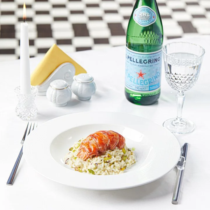 Elegant dining setting with lobster risotto, San Pellegrino bottle, candle, and glassware.