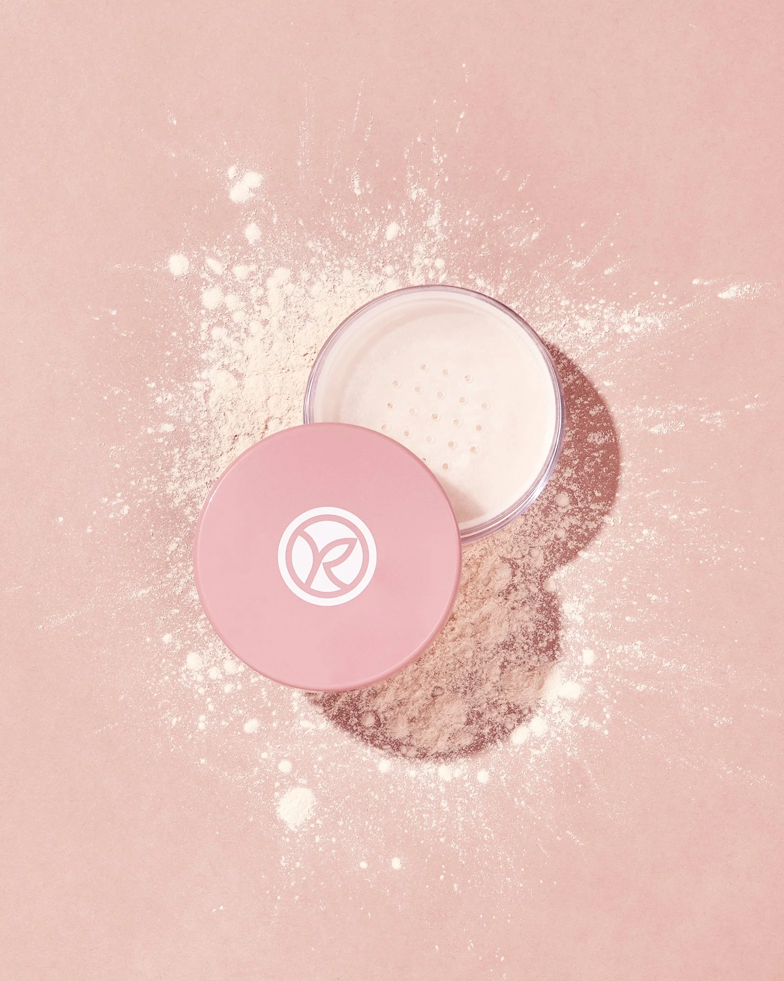 Pembe fonda, çevresine dağılmış pudra ile birlikte açık bir yüz pudrası kabı.