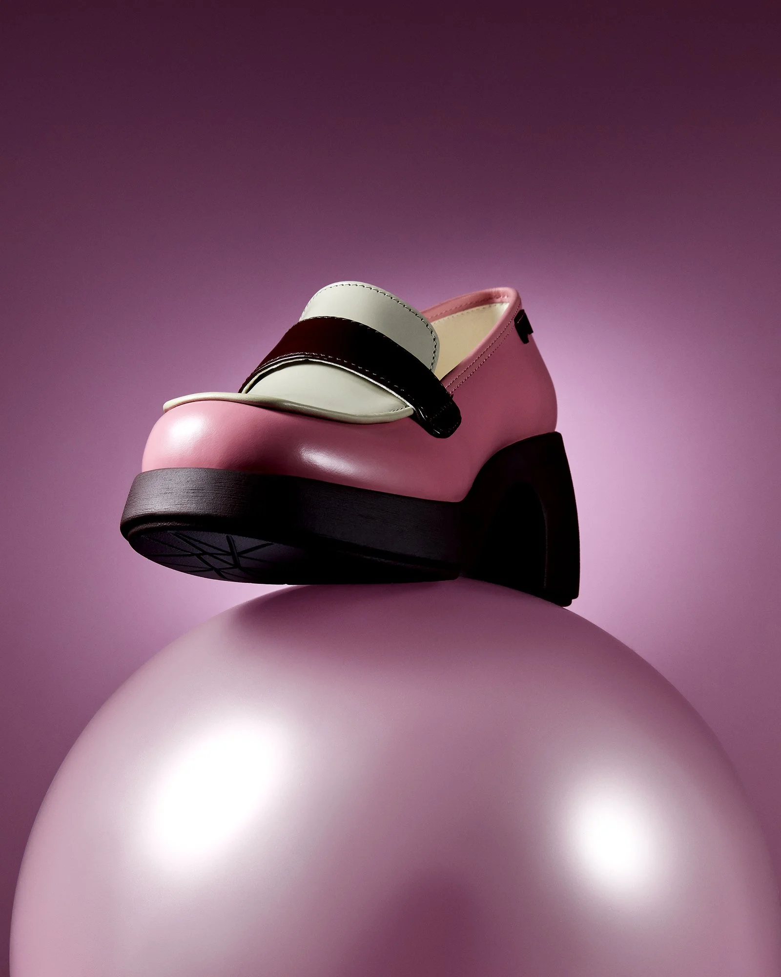 Kalın siyah topuklu, pembe gövdeli ve üst kısmında kayışı olan şık bir ayakkabı; büyük pembe küresel bir objenin üzerinde, pembe gradyan bir arka planla sergileniyor.