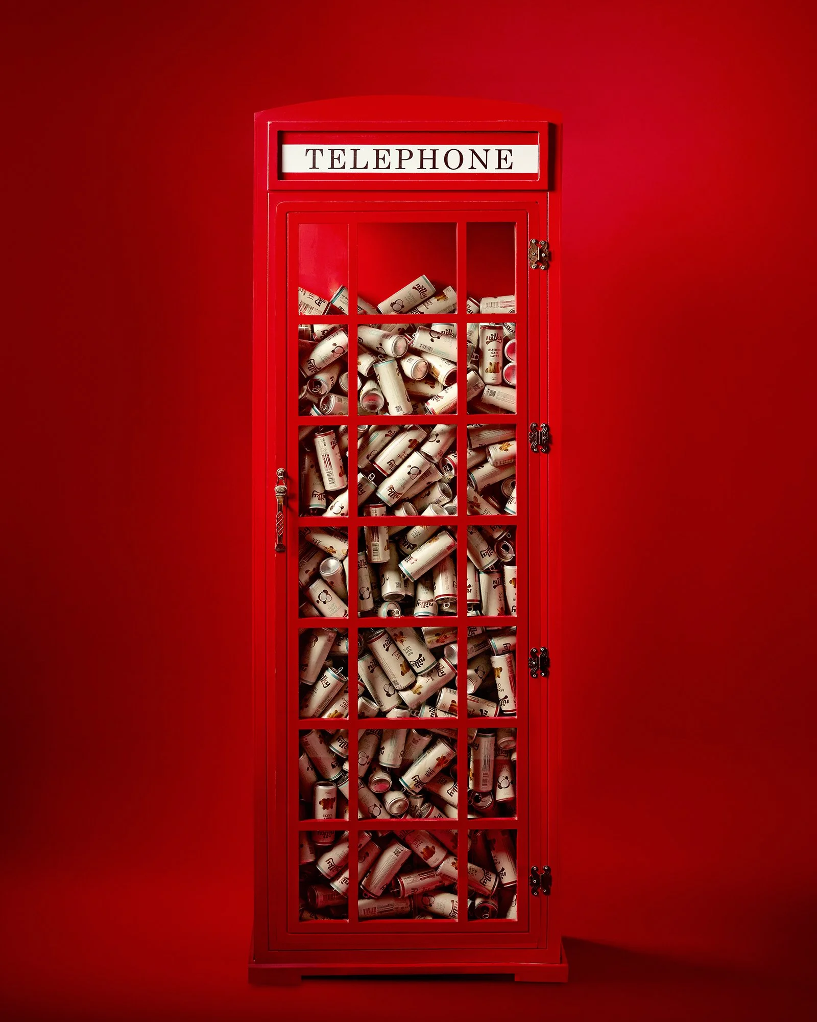Kırmızı bir arka plan önünde, içi ezilmiş alüminyum kutularla dolu kırmızı vintage bir telefon kulübesi.