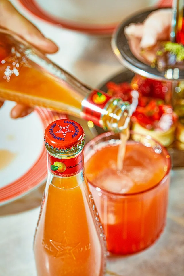 Portakal sodasının buz dolu bir bardağa dökülmesi, etrafında bir şişe ve tatlı tepsisi bulunuyor.

