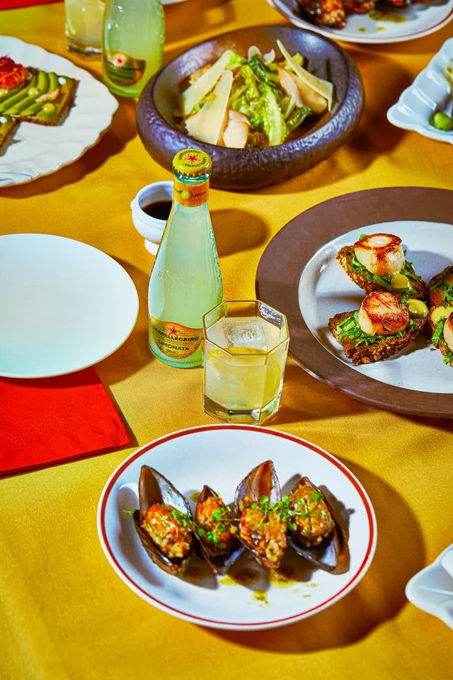 Deniz ürünleri, salata, açık içecek şişesi ve bardaklarla süslenmiş masa düzeni.

