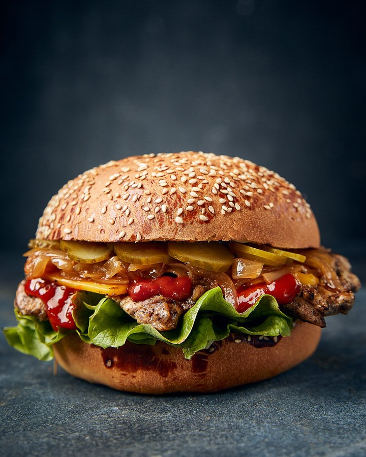 Gourmet hamburger with sesame seed bun, lettuce, caramelized onions, pickles, and ketchup.