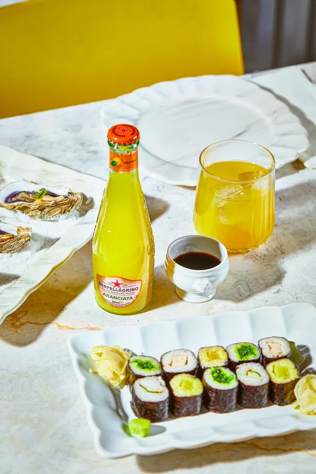 Kuşkonmaz ve prosciutto ile süslenmiş beyaz tabakta gurme yemek, yanında bir şişe maden suyu.

