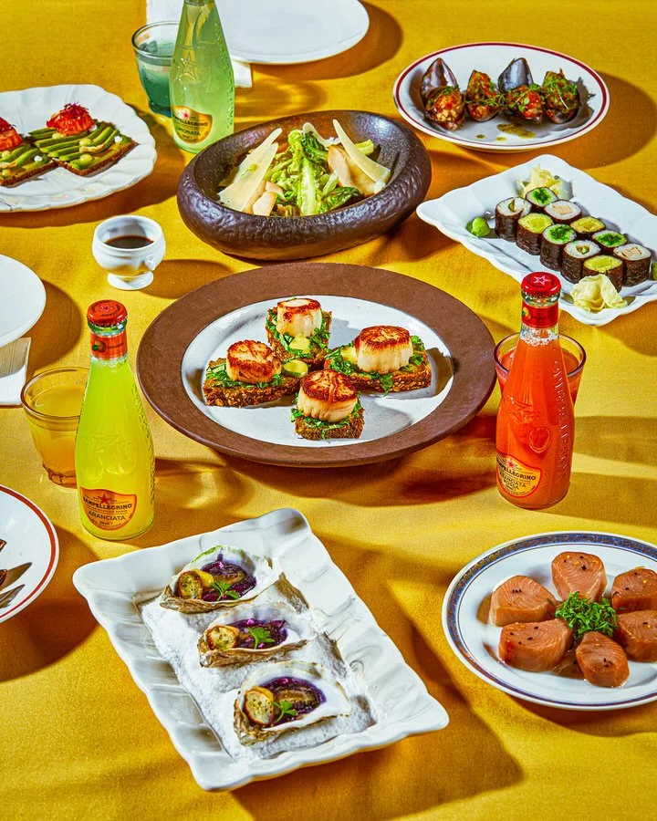 Gurme yemeklerin yer aldığı masa düzeni, otlarla süslenmiş deniz tarağı, suşi ruloları, ızgara sebzeler, köfte, garnitürlü istiridyeler ve somon dilimleri içeriyor.

