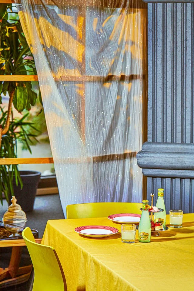 Sarı masa örtüsü üzerinde bir şişe gazlı içecek ve bir bardak içecek bulunan masa düzeni.

