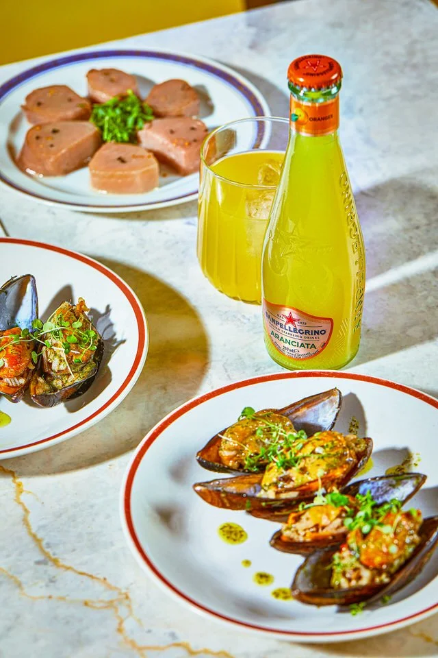 Ot tabağı ve dilimlenmiş et tabağı, yanında bir şişe gazlı içecek ve portakal içeceği bulunan masa düzeni.