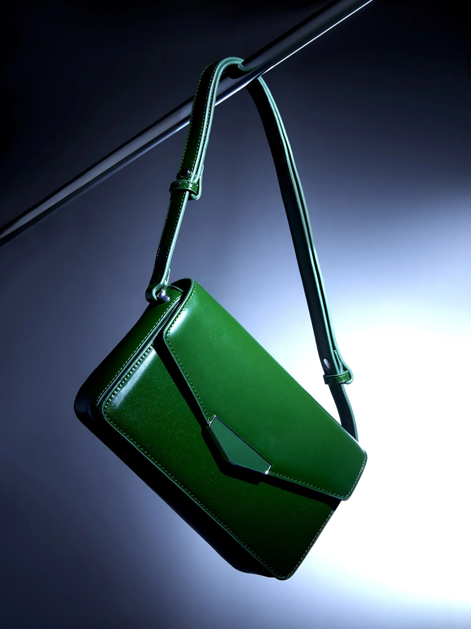 Koyu bir arka plan önünde, spot ışığı efektiyle aydınlatılmış bir çubuktan sarkan parlak yeşil bir çanta.