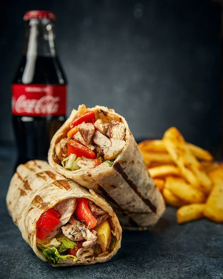 Koyu arka planda sebzelerle doldurulmuş ızgara tavuk dürüm, yanında bir şişe içecek ve patates kızartması.

