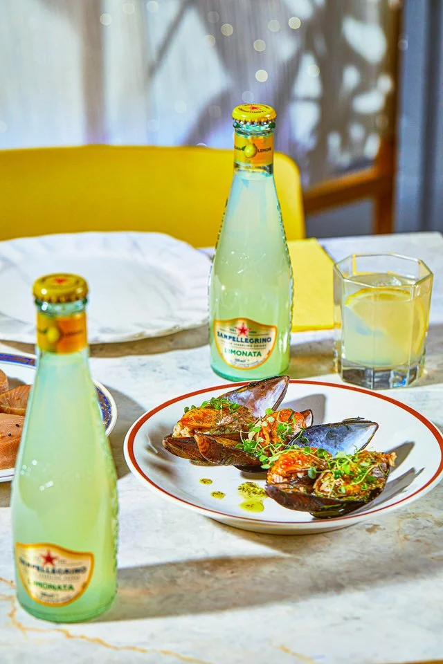 Baharatlı midye tabağı, yanında iki şişe limonata ve bir bardak limon içeceği bulunan masa düzeni.

