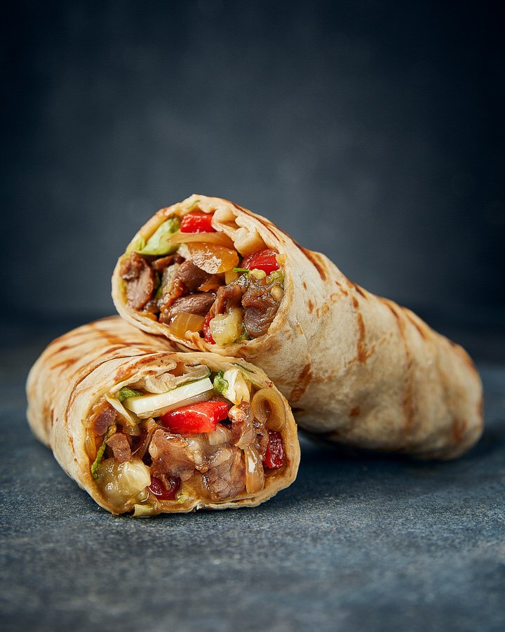 Two sliced shawarma wraps with meat and vegetables on a dark background.