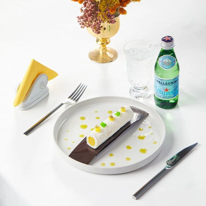 Gurme yemek tabakları, kristal bardaklar ve dekoratif bitkilerle süslenmiş şık bir yemek masası düzeni.

