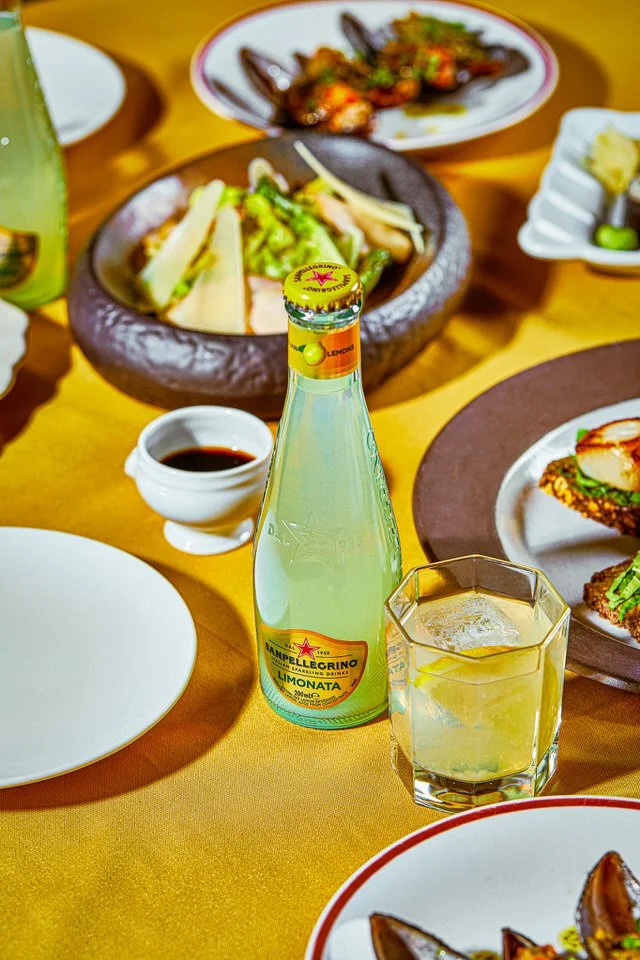 Sarı masa örtüsü üzerinde bir şişe limonata ve yemek tabakları.

