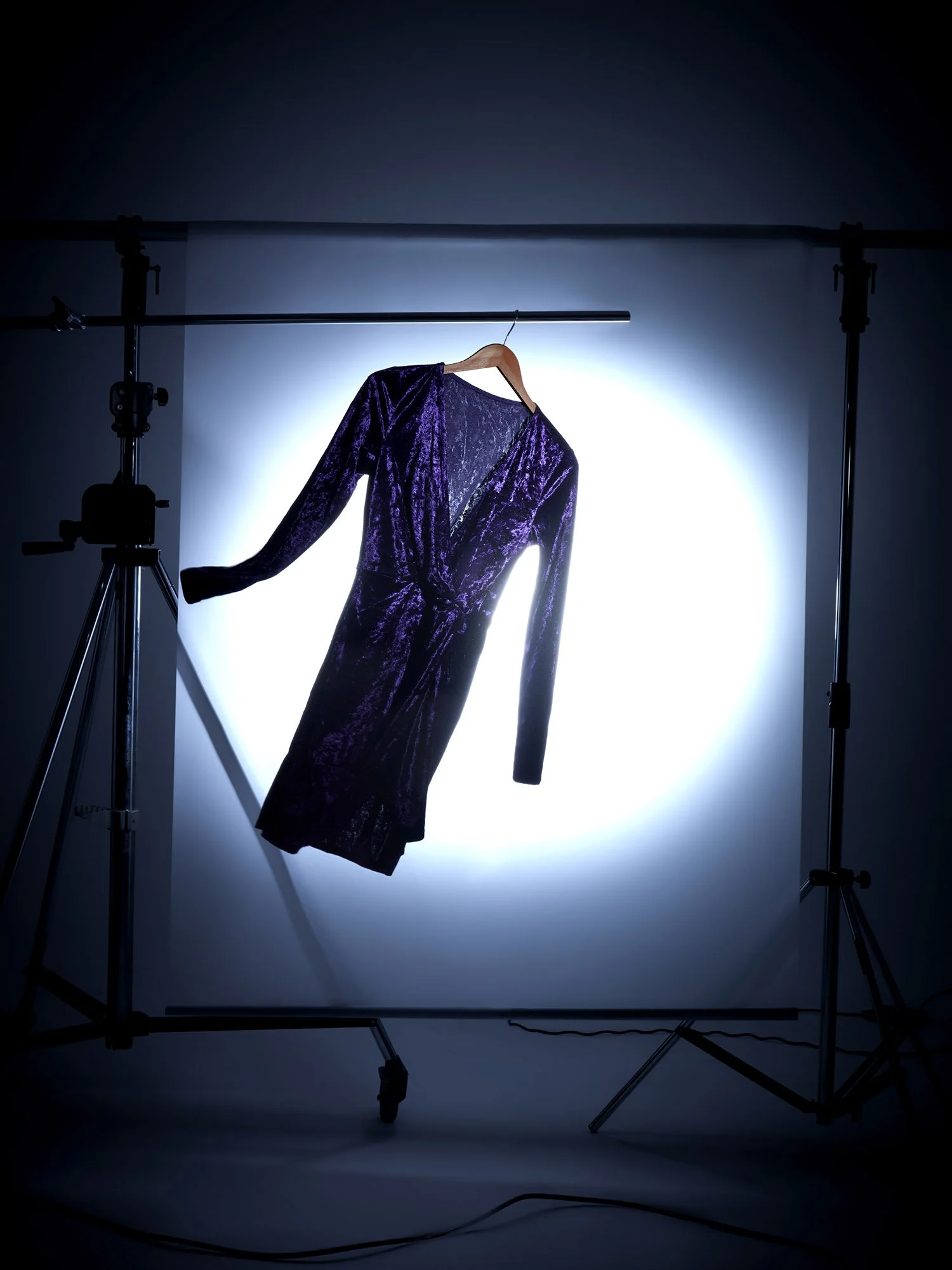 Bir fotoğraf stüdyosunda, arka ışıklandırma ve ekipmanların arasında askıda duran mor kadife bir elbise.