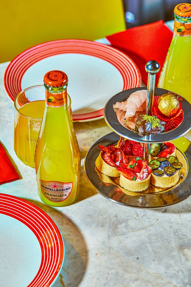 İki katlı tatlı tepsisi, portakal suyu bardakları ve kırmızı-beyaz kenarlı tabaklarla süslenmiş masa düzeni.
