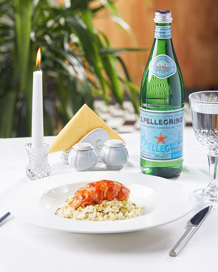 Şık bir yemek masasında iki tabakta gurme yemek sunumu. Beyaz masa örtüsü üzerinde özenle hazırlanmış yemekler, kristal bardaklar ve buz kovasında şişeler bulunuyor.

