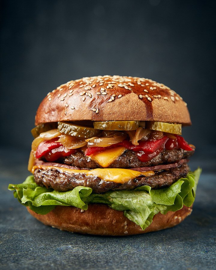 Gourmet cheeseburger with lettuce, pickles, grilled onions, and red peppers on a sesame seed bun.