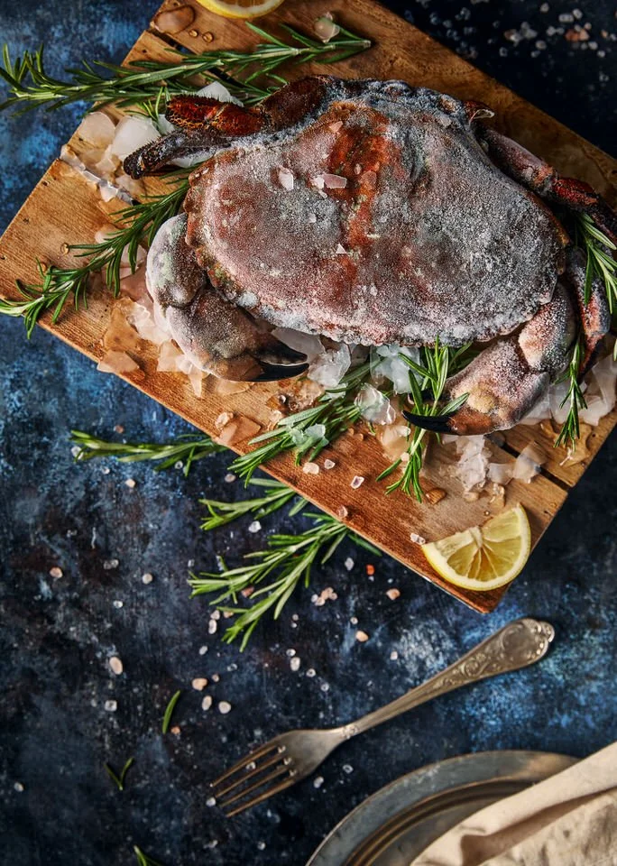 Buz, biberiye ve limon dilimleriyle süslenmiş ahşap bir tahtada dondurulmuş yengeç.
