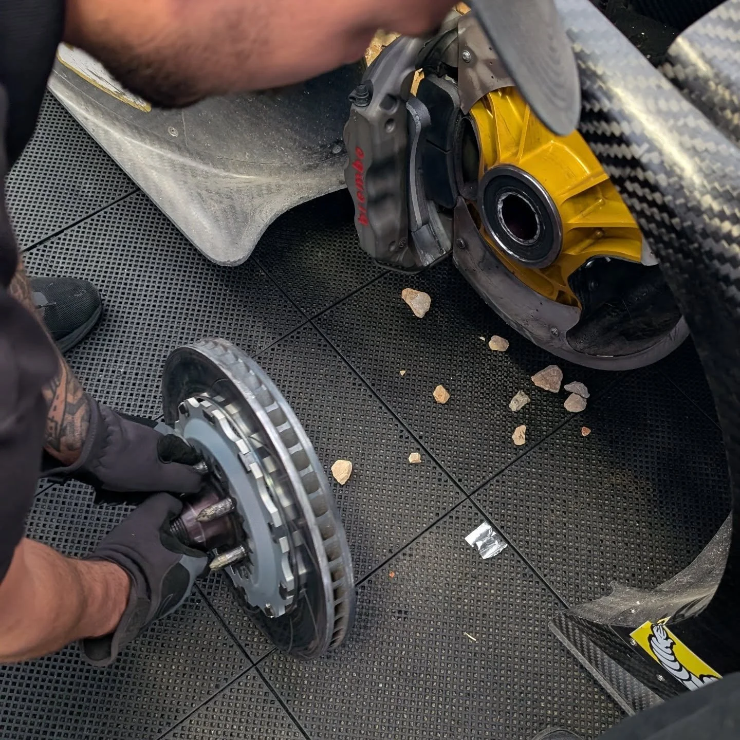 A person working on removing or installing a brake rotor and caliper on a high-performance sports car, with the car's wheel hub visible.