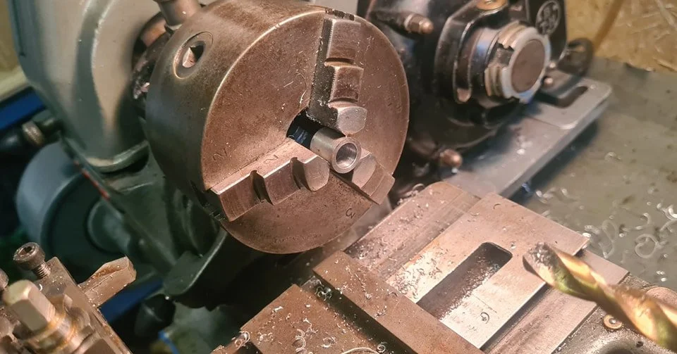 Close-up of a metal lathe machine with a rotating chuck holding a metal workpiece, in a machine shop setting.