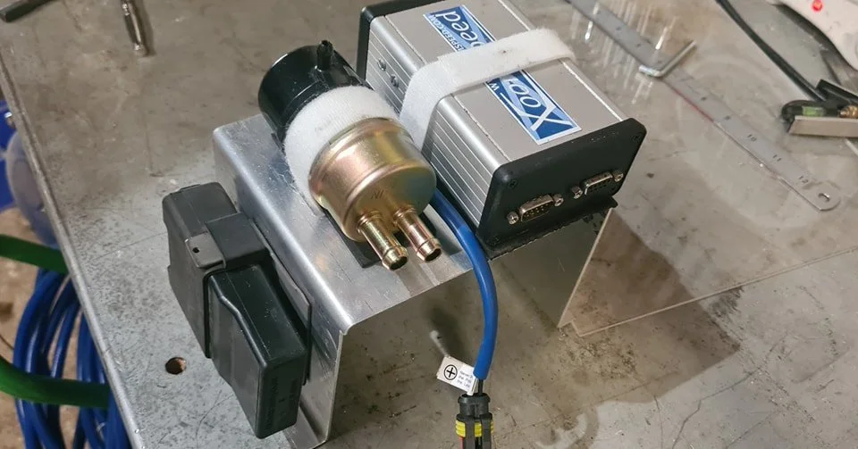 Electronic components on a metallic surface, including a black and gold cylindrical device, two silver modules with blue labels, and a blue cable attached to a small circuit board.