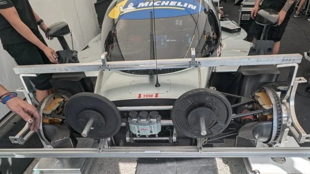 Race car in the pit stop with team members working on it, pit lane background, during a motorsport event.