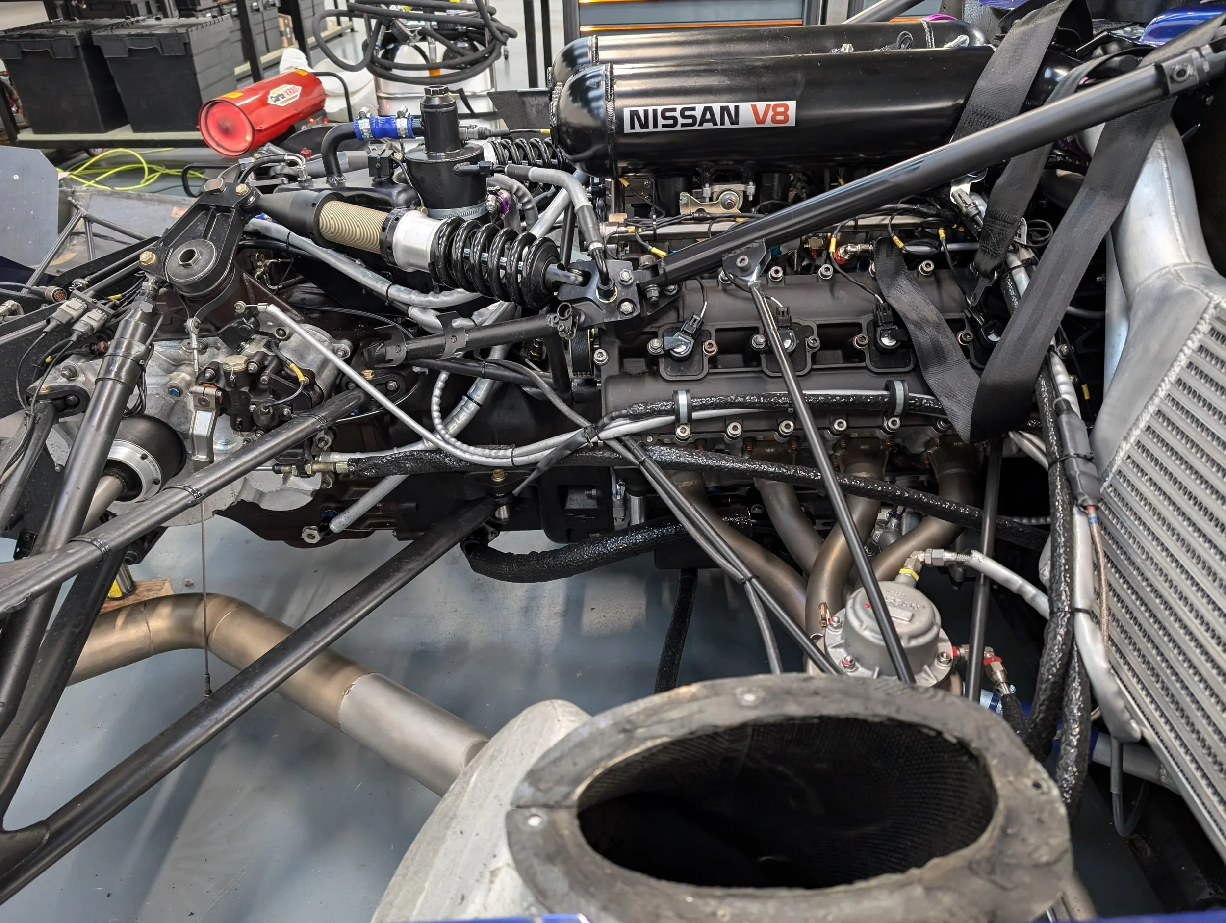 Close-up of a car engine with various components, including a Nissan V8 engine, radiator, and intricate wiring and piping.