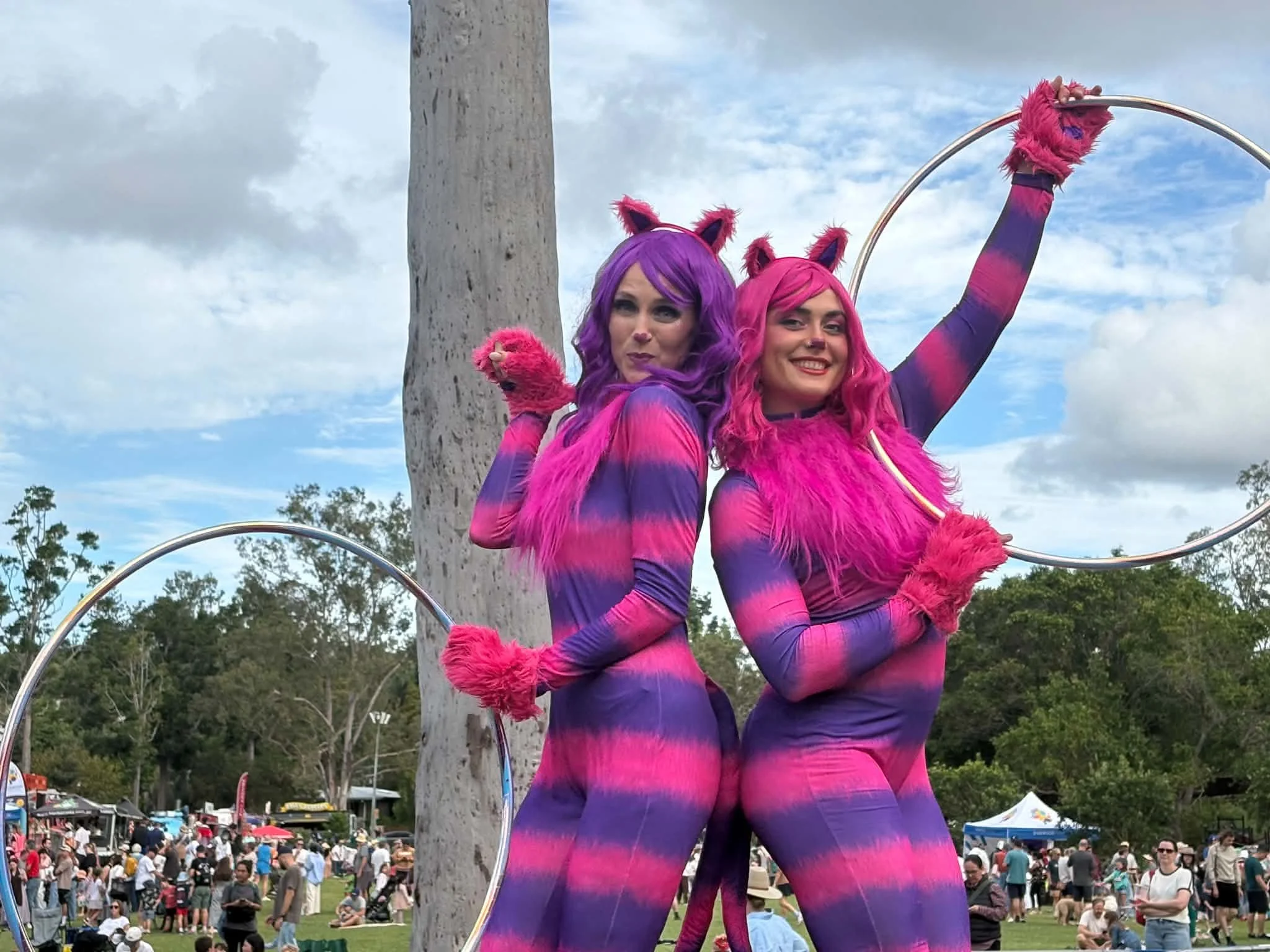 Pink and purple cat stilt walkers performing with hoops at an outdoor Brisbane festival.