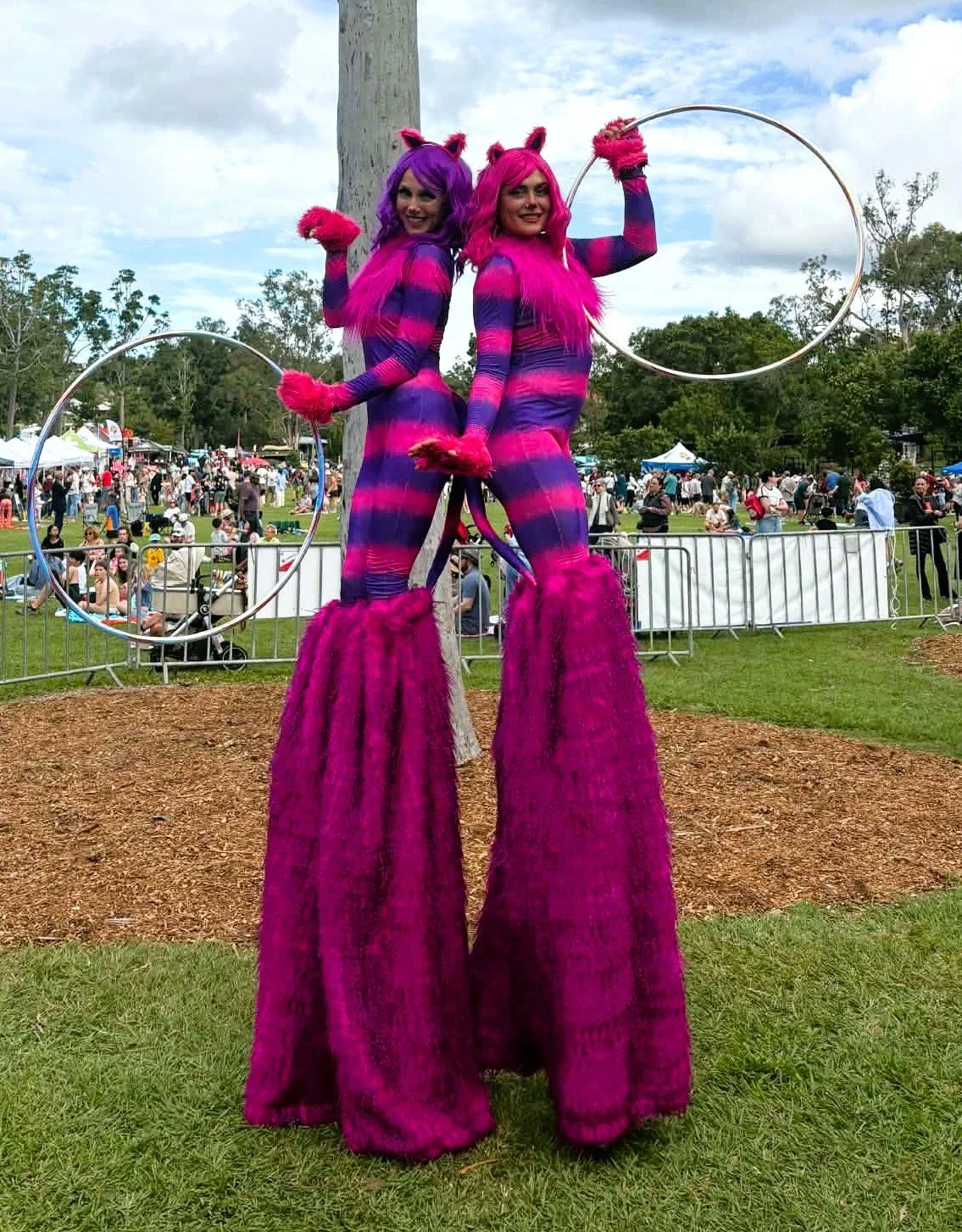 Roving stilt walkers in bold pink and purple costumes providing entertainment at a Queensland event