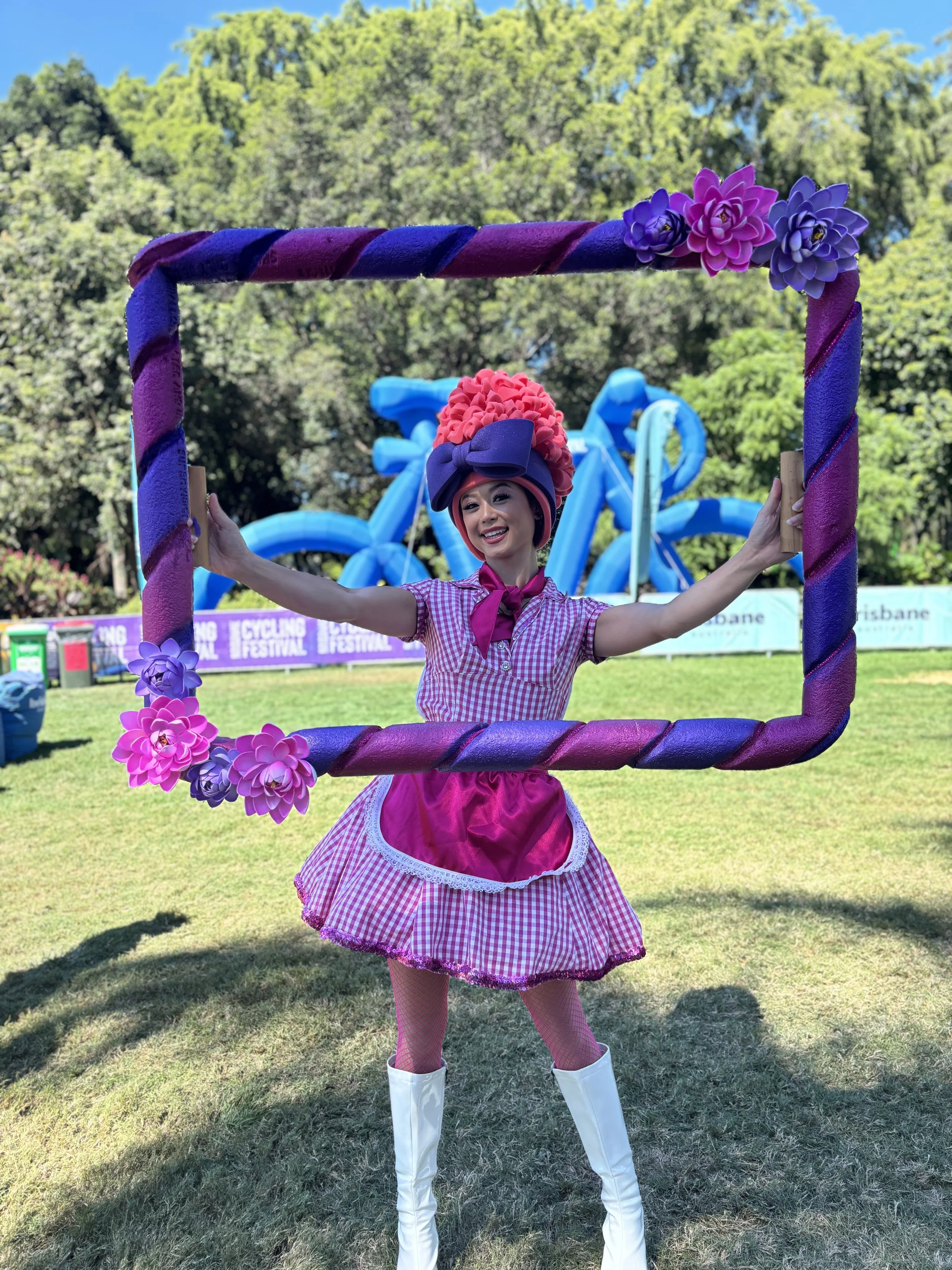 Roving festival performer holding a custom pink and purple picture frame for interactive guest photos at outdoor event